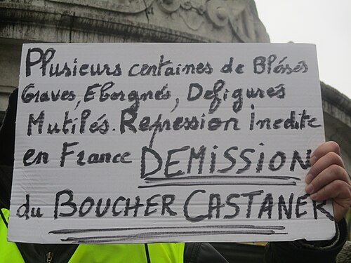Banderole « Castaner gangster » tenue au-dessus d'un cortège parisien.