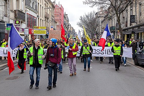 Cortège de gilets jaunes et de drapeaux syndicaux dans une rue de Bordeaux.