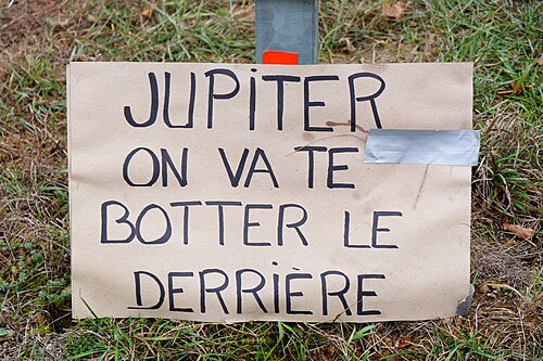 Pancarte en carton « Jupiter, on va te botter le derrière » plantée au bord d'une route.