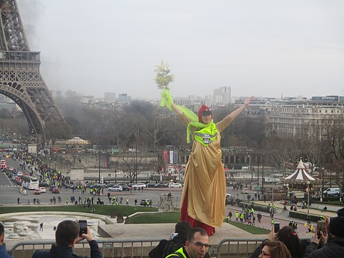 Un manifestant en gilet jaune debout sur un socle au Trocadéro, dans la brume.